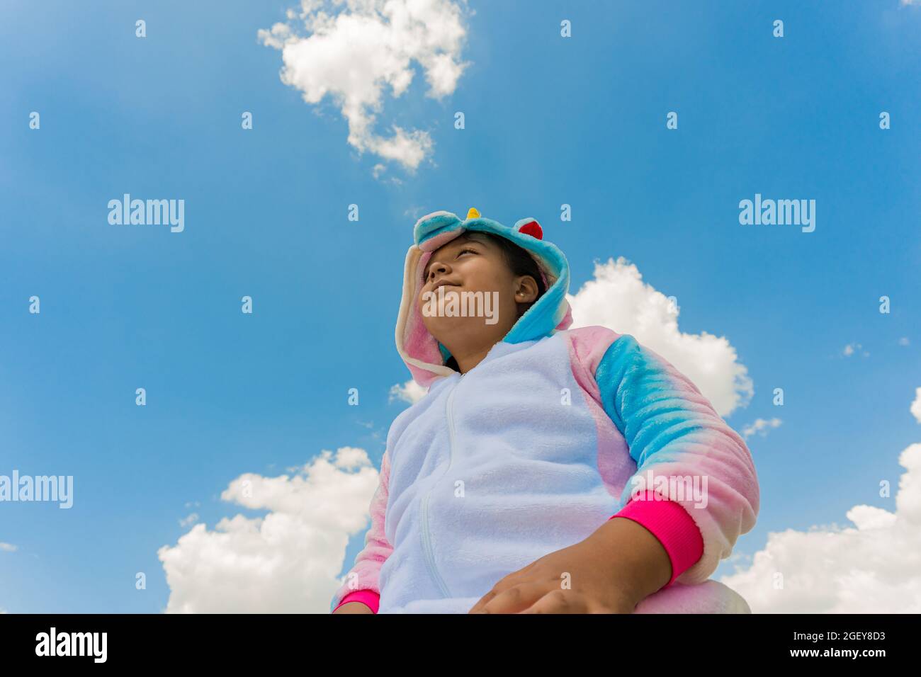 Nahaufnahme eines glücklichen hispanischen Jungen in einem Einhorn-Kostüm und blauem Himmel auf dem Hintergrund Stockfoto