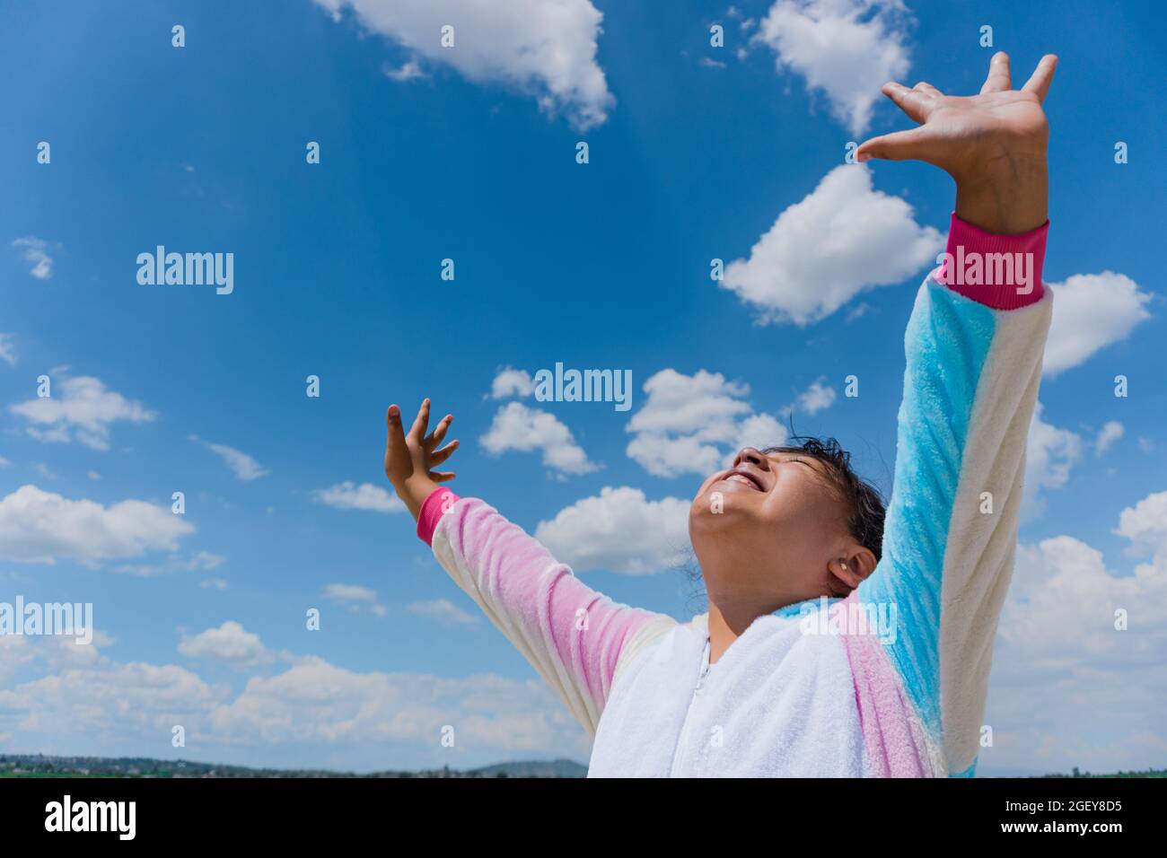 Nahaufnahme eines glücklichen hispanischen Jungen mit ausgestreckten Armen und blauem Himmel im Hintergrund Stockfoto