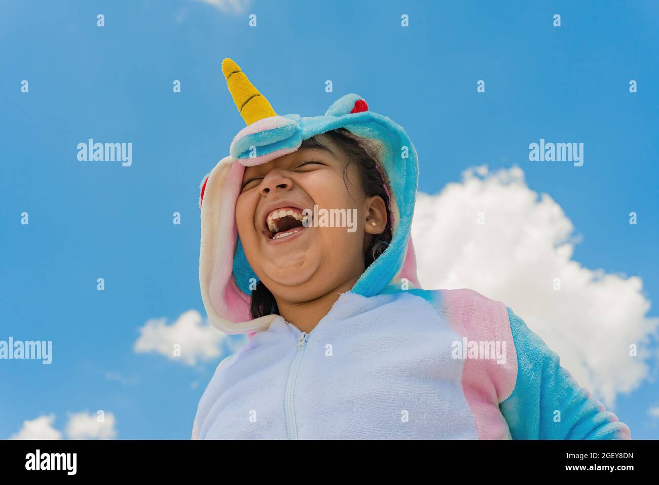 Nahaufnahme eines glücklichen hispanischen Jungen in einem Einhorn-Kostüm und blauem Himmel auf dem Hintergrund Stockfoto