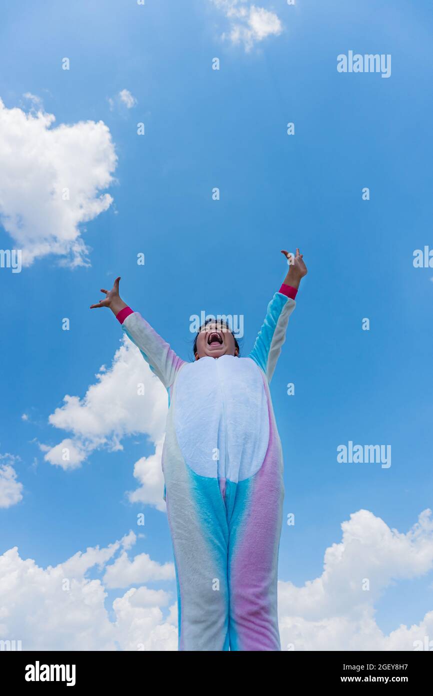 Eine vertikale Aufnahme eines glücklichen hispanischen Jungen mit ausgestreckten Armen und blauem Himmel auf dem Hintergrund Stockfoto