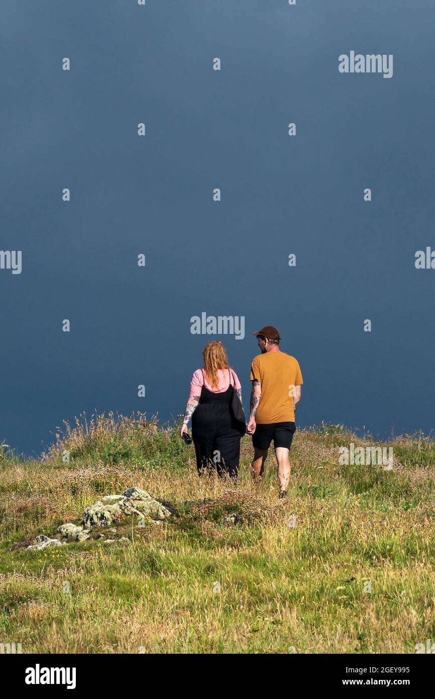 Die Rückansicht eines Paares, das auf dem Pentire Point East unter einem dunklen bedrohlichen Himmel in Newquay in Cornwall läuft. Stockfoto