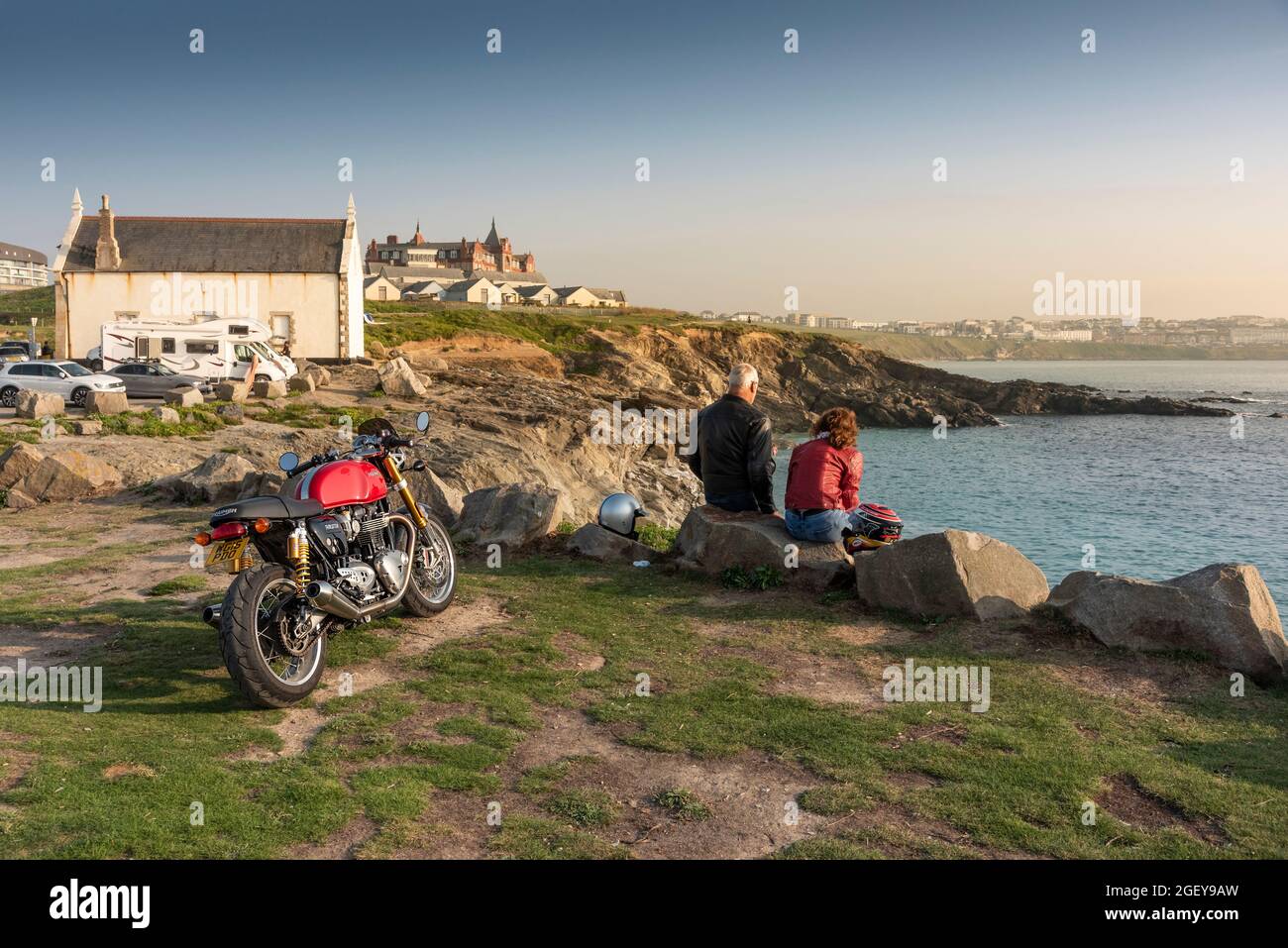 Ein Motorradfahrer und sein Sozius sitzen auf Felsen mit Blick auf Little Fistral in Newquay in Cornwall. Stockfoto
