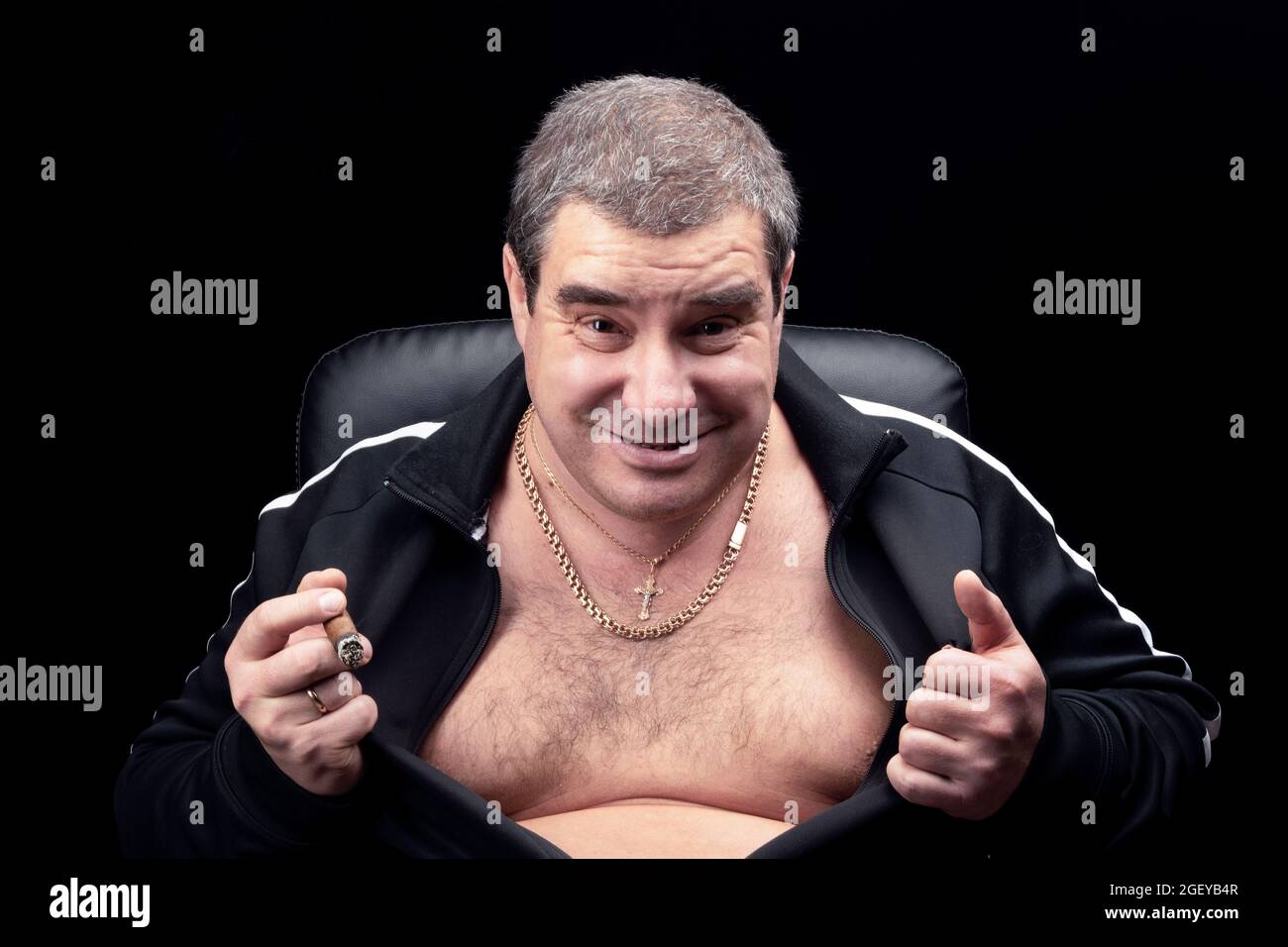 Ein lustiger, fetter Mann reißt sein Hemd auf seine Brust. Eine kriminelle Autorität bei einem Bandenvorkampf, eine lustige Parodie. Ein Grimasse oder ein Lächeln auf seinem Gesicht. Stockfoto
