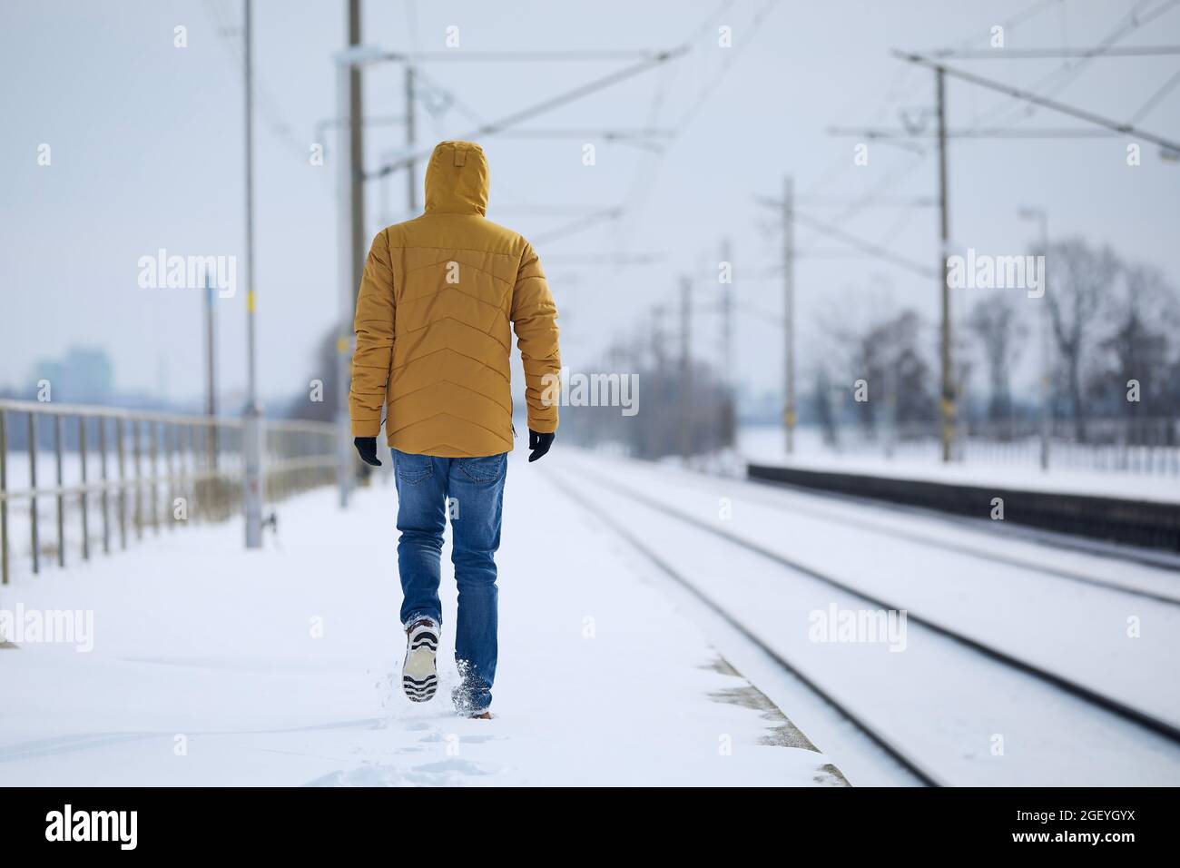 Rückansicht der einsamen Person in warmer Kleidung. Der Mann verlässt den Bahnhof vor einer verschneiten Landschaft. Stockfoto