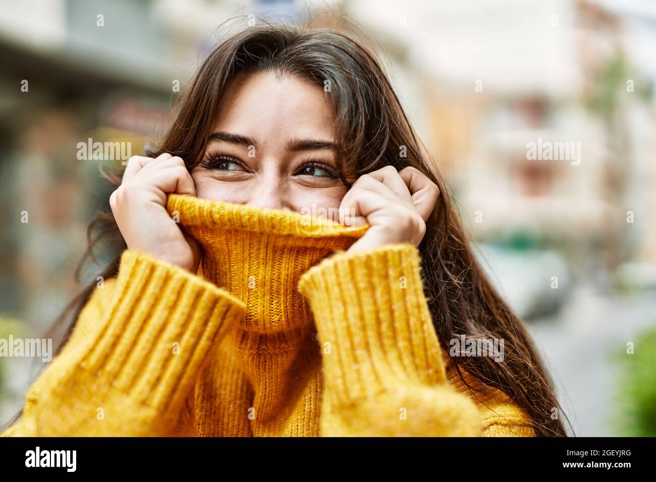 Junge schöne Brünette Frau trägt Rollkragenpullover dabei lustige Geste,  die Gesicht mit Pullover bedeckt Stockfotografie - Alamy