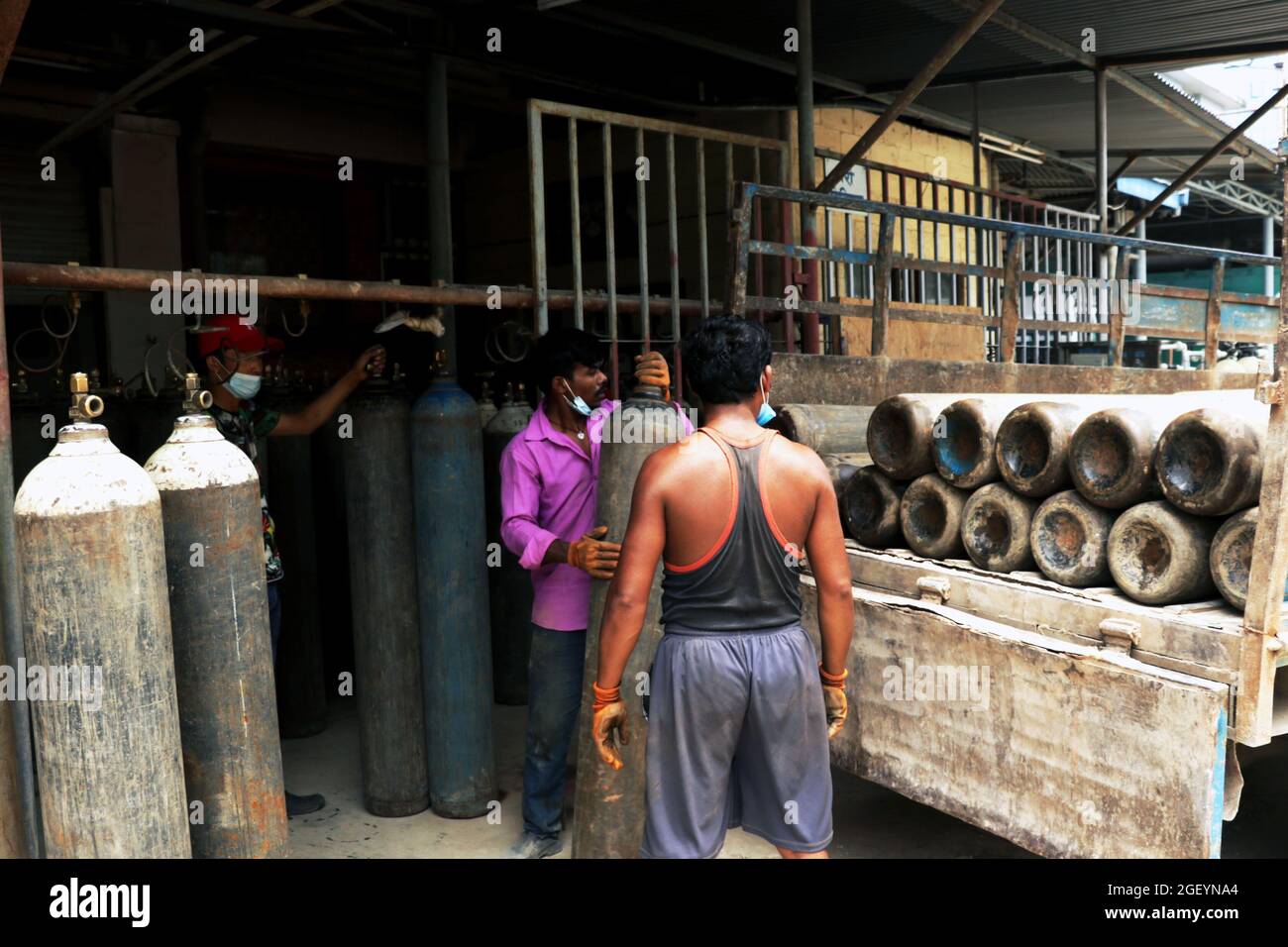 Drei Arbeiter beladen leere Sauerstoffflaschen in den LKW, um ihn zum Nachfüllen zu bringen. Stockfoto