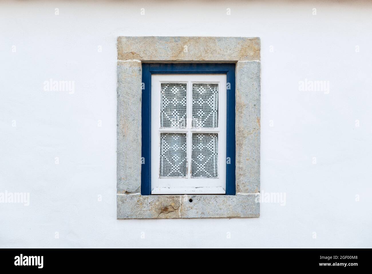 Detail eines traditionellen Fensters auf einer weißen Fassade eines Hauses, mit Häkelvorhängen, in Portugal. Stockfoto