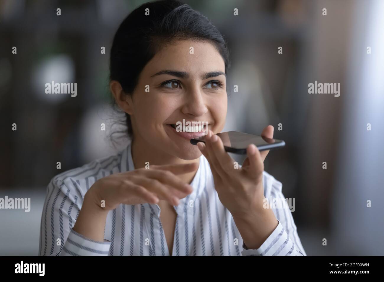Lächelnde Inderin zeichnet Audionachrichten auf dem Handy auf Stockfoto