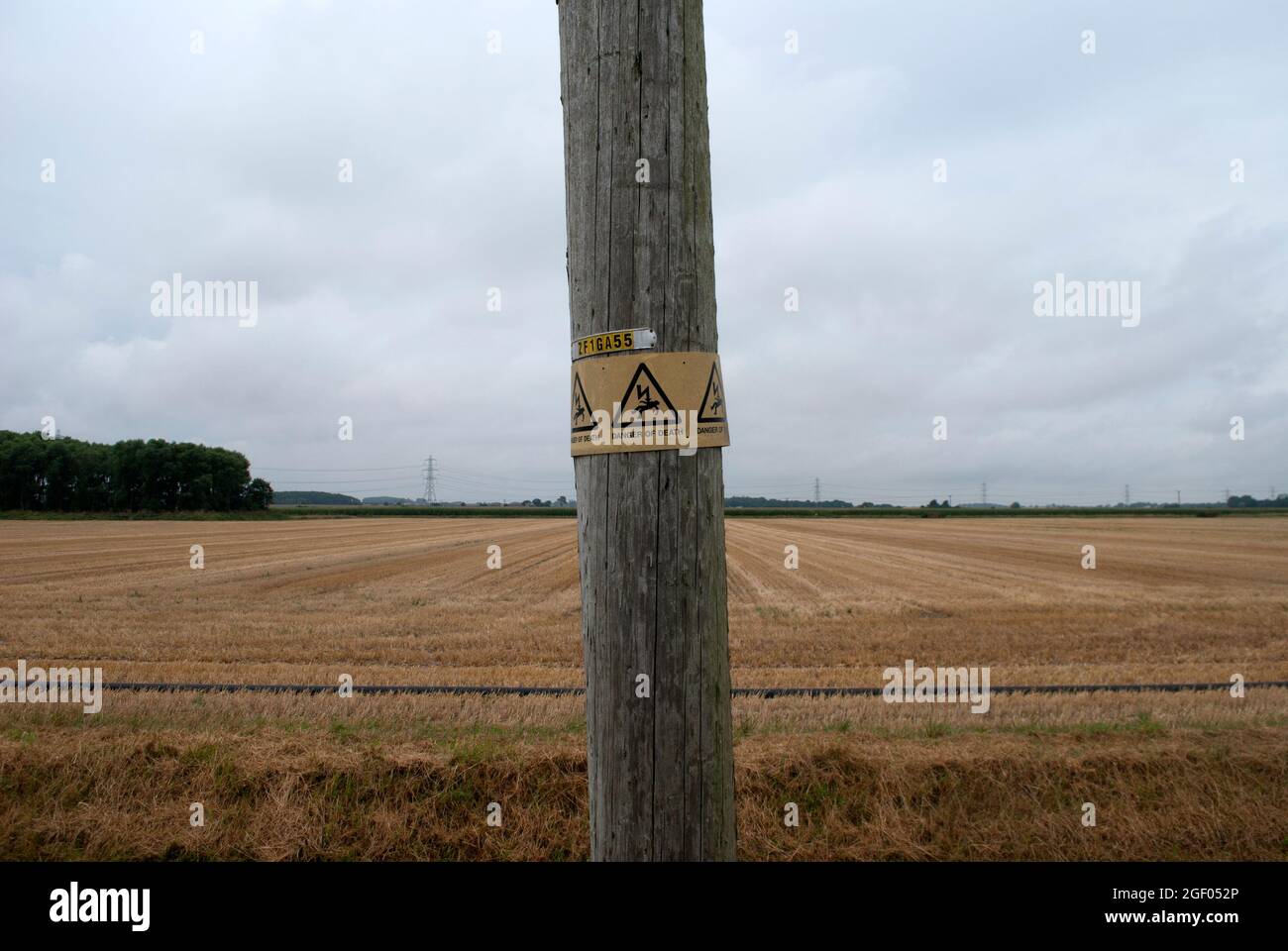 Schild Todesgefahr auf dem Telegrafenmast vor dem mit Stoppeln gefüllten Feld Stockfoto