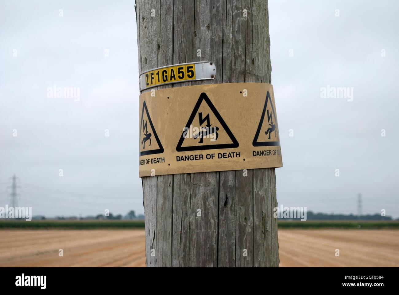 Schild Todesgefahr auf dem Telegrafenmast vor dem mit Stoppeln gefüllten Feld Stockfoto