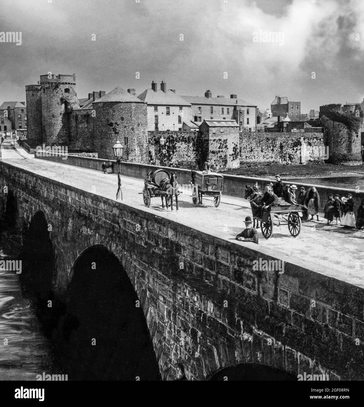 Eine Ansicht von Pferdefahrzeugen und Menschen aus dem frühen 20. Jahrhundert auf der Thormond Bridge über dem Fluss Shannon, die vom König John's Castle aus dem 13. Jahrhundert, Stadt Limerick, Irland, überragt wird Stockfoto