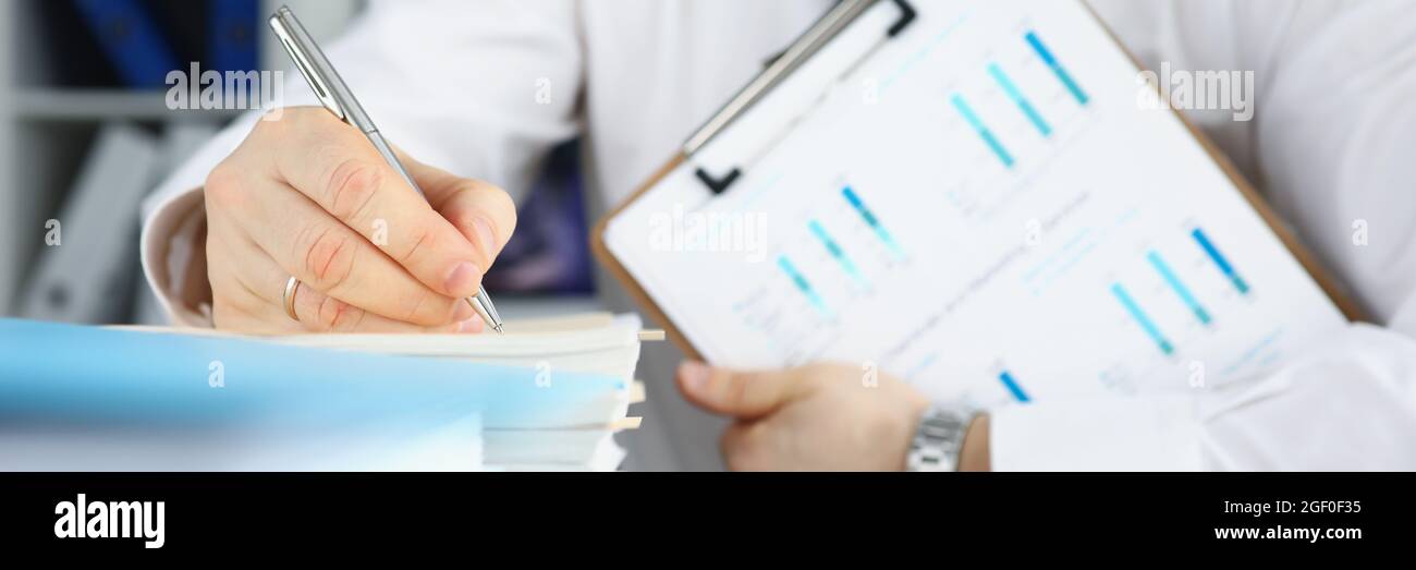 Geschäftsmann hält Zwischenablage mit kommerziellen Charts in seinen Händen und Macht Notizen in Dokumenten Stockfoto