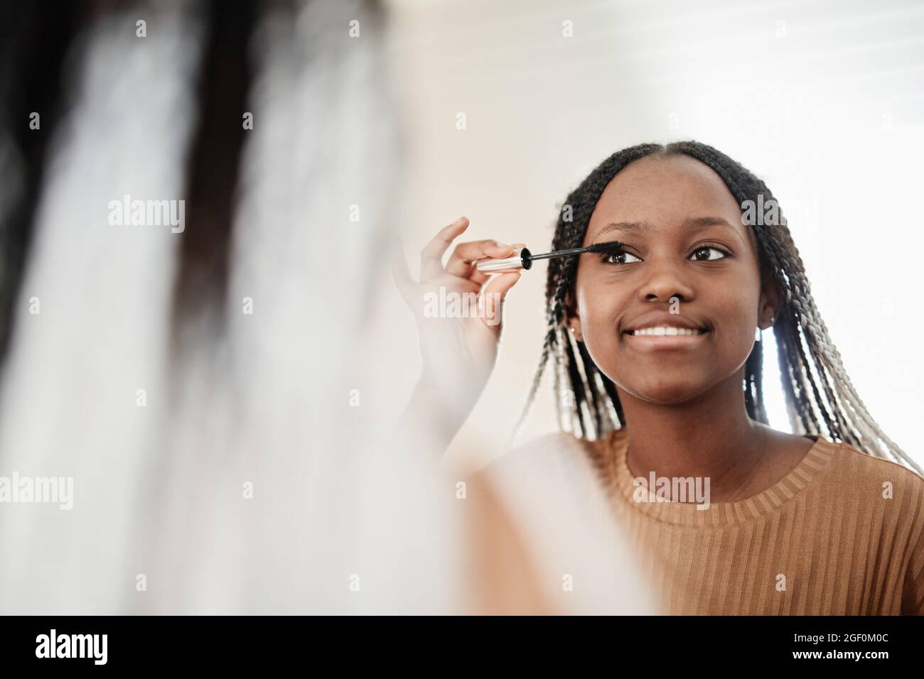 Porträt einer jungen afroamerikanischen Frau, die morgens Mascara aufsetzt, während sie sich schminkt und den Spiegel und den Kopierraum anschaut Stockfoto