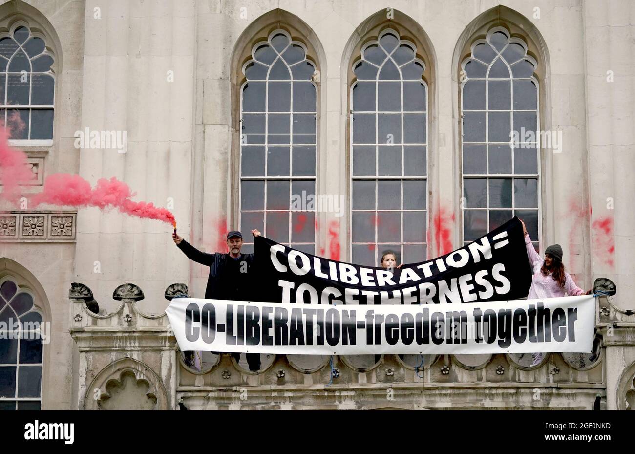 Menschen lassen Fackeln los und entrollen ein Banner von einem Vorsprung über dem Eingang zur Guildhall in London, während die Extinction Rebellion einen Protest ausführt. Bilddatum: Sonntag, 22. August 2021. Stockfoto