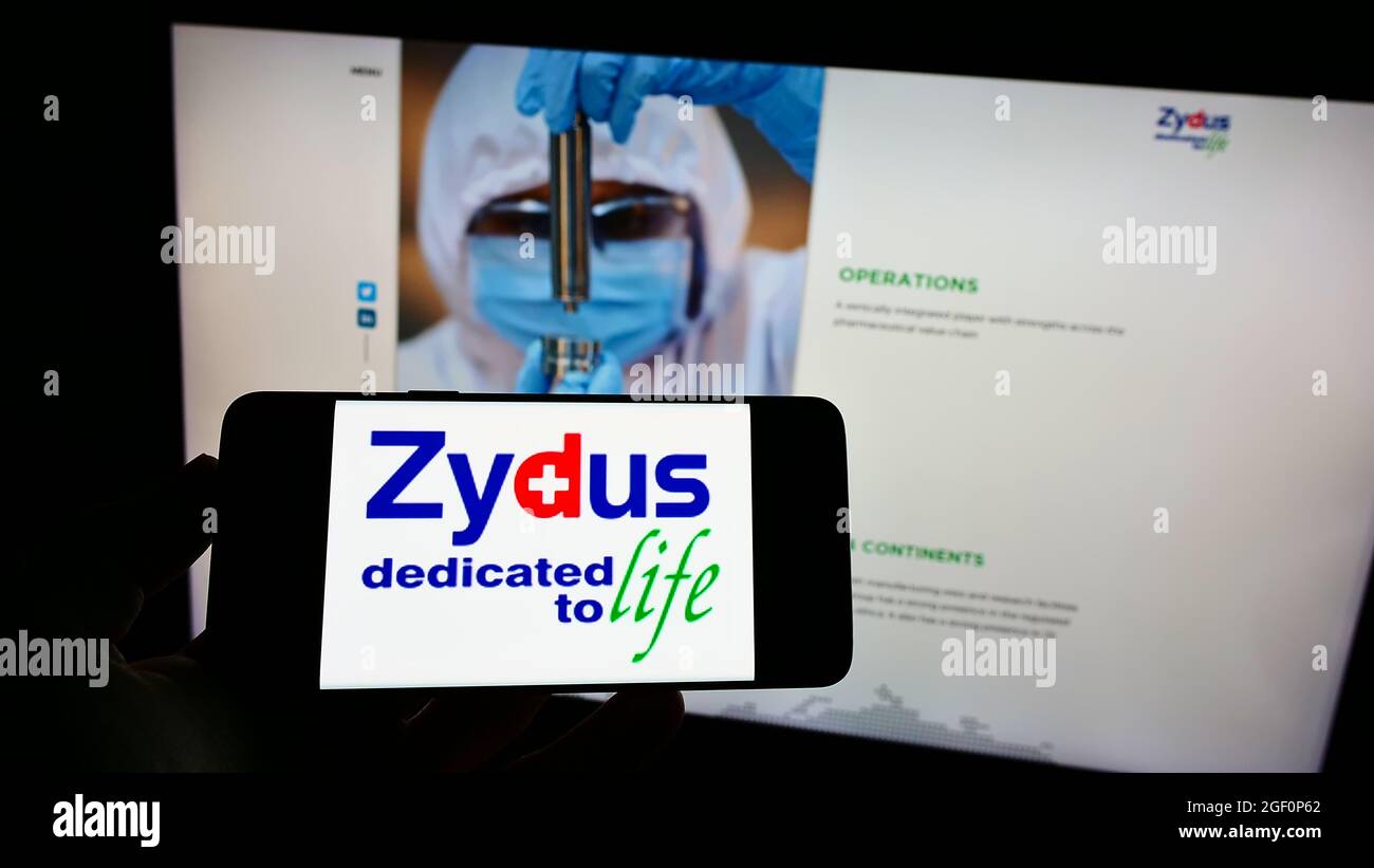 Person mit Mobiltelefon und Logo des indischen Unternehmens (Zydus) Cadila Healthcare Limited auf dem Bildschirm vor der Webseite. Konzentrieren Sie sich auf die Telefonanzeige. Stockfoto