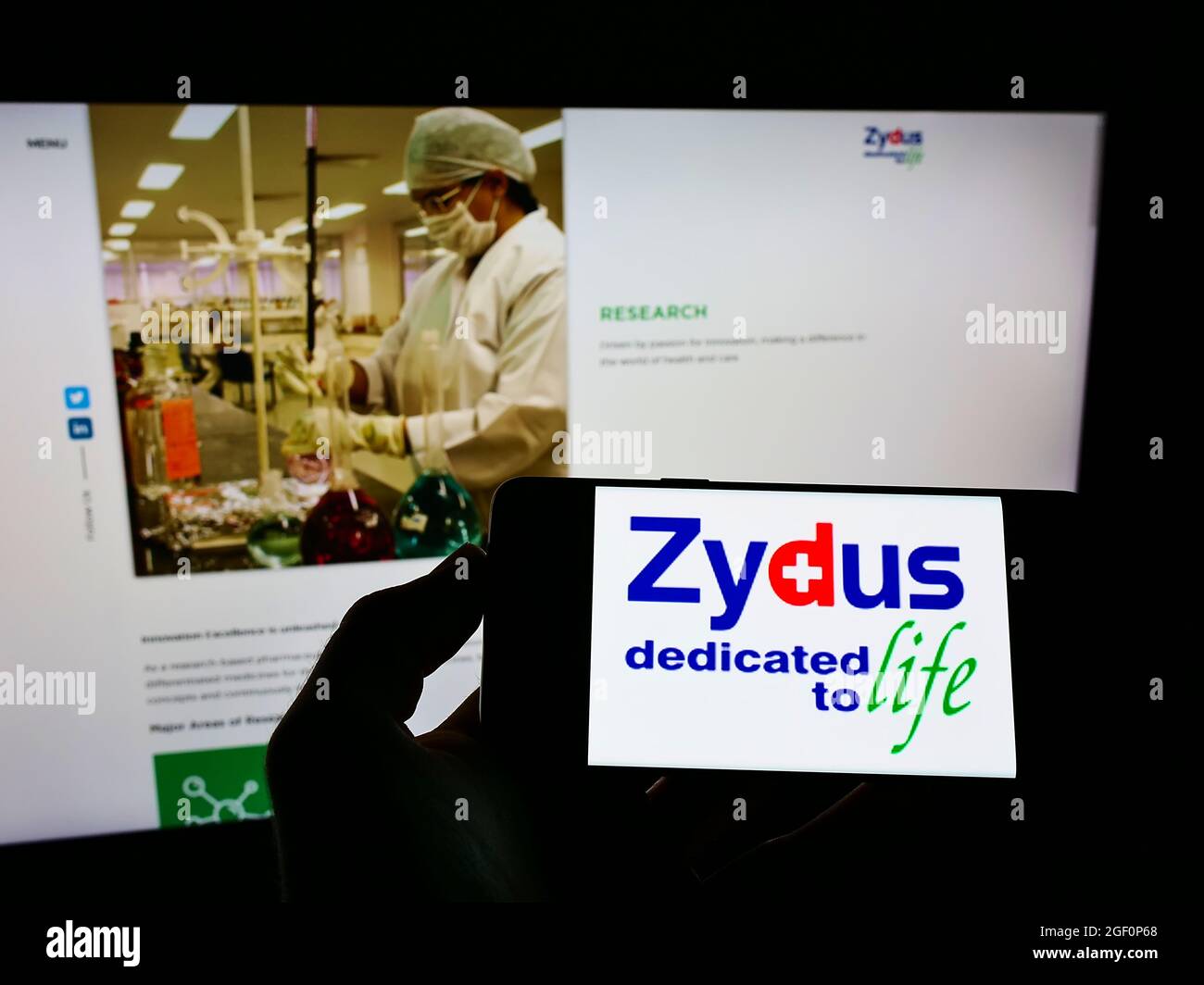 Person mit Mobiltelefon und Logo des indischen Unternehmens (Zydus) Cadila Healthcare Limited auf dem Bildschirm vor der Webseite. Konzentrieren Sie sich auf die Telefonanzeige. Stockfoto