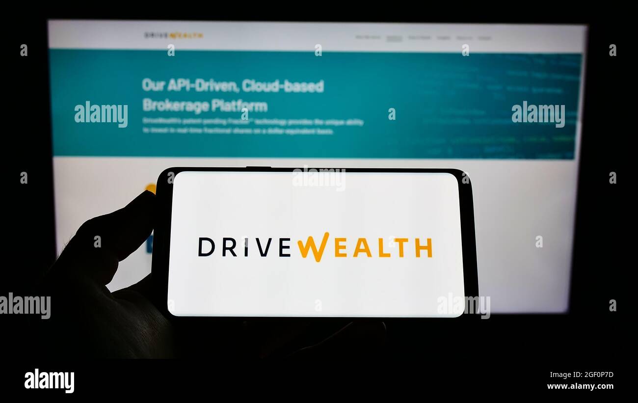 Person, die Mobiltelefon mit dem Logo des amerikanischen Fintech-Unternehmens DriveWealth LLC auf dem Bildschirm vor der Webseite hält. Konzentrieren Sie sich auf die Telefonanzeige. Stockfoto
