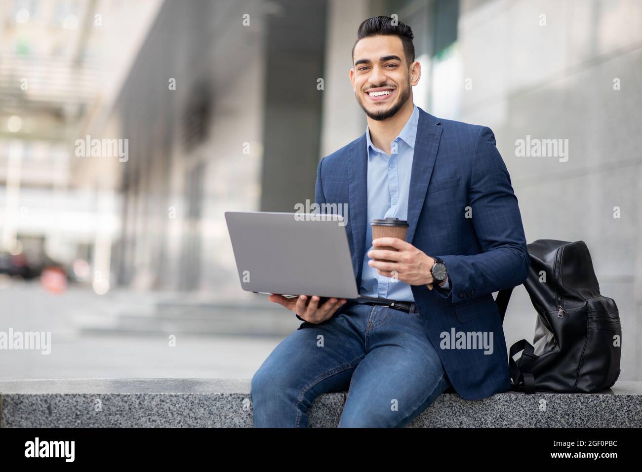Positiver Typ aus dem Nahen Osten mit Laptop, der eine Kaffeepause im Freien hat Stockfoto