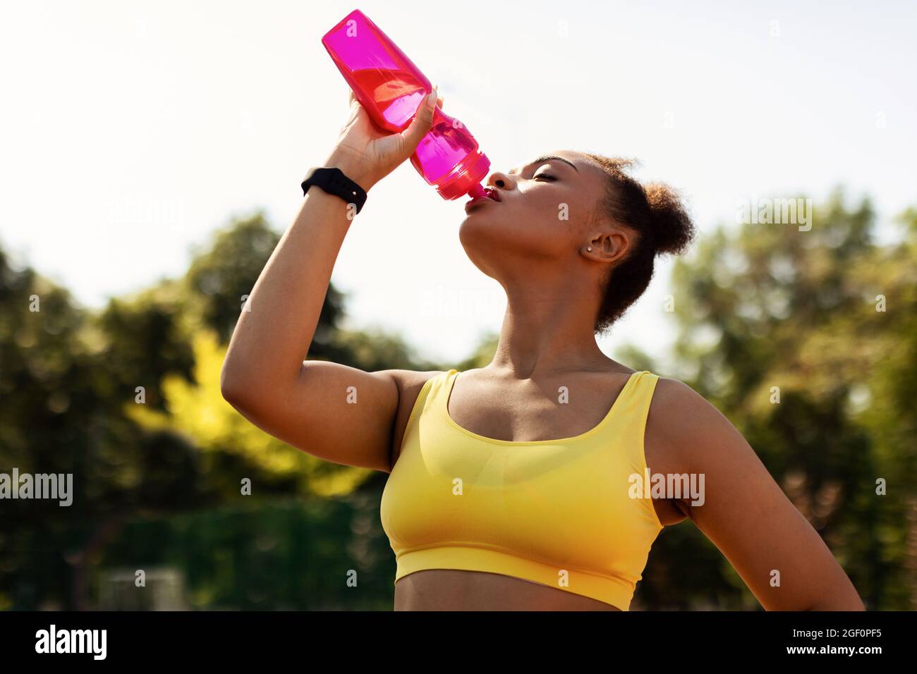 Porträt einer sportlichen schwarzen Frau in gelbem Sportswear-Trinkwasser Stockfoto