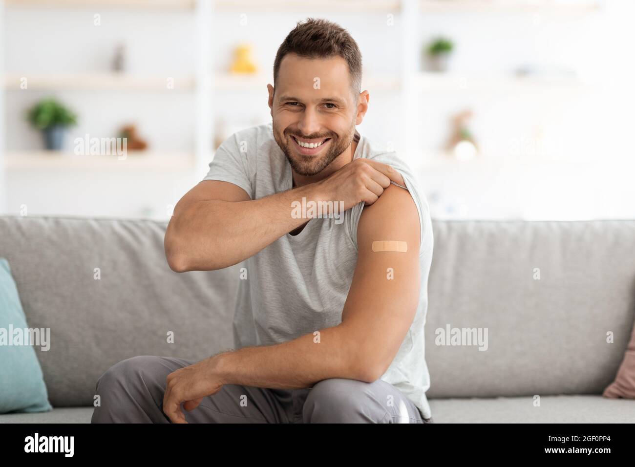 Glücklicher junger, geimpfter Mann, der nach der Impfstoffinjektion die Schulter mit medizinischem Gips zeigte und mit einem breiten Lächeln vor der Kamera lächelte Stockfoto