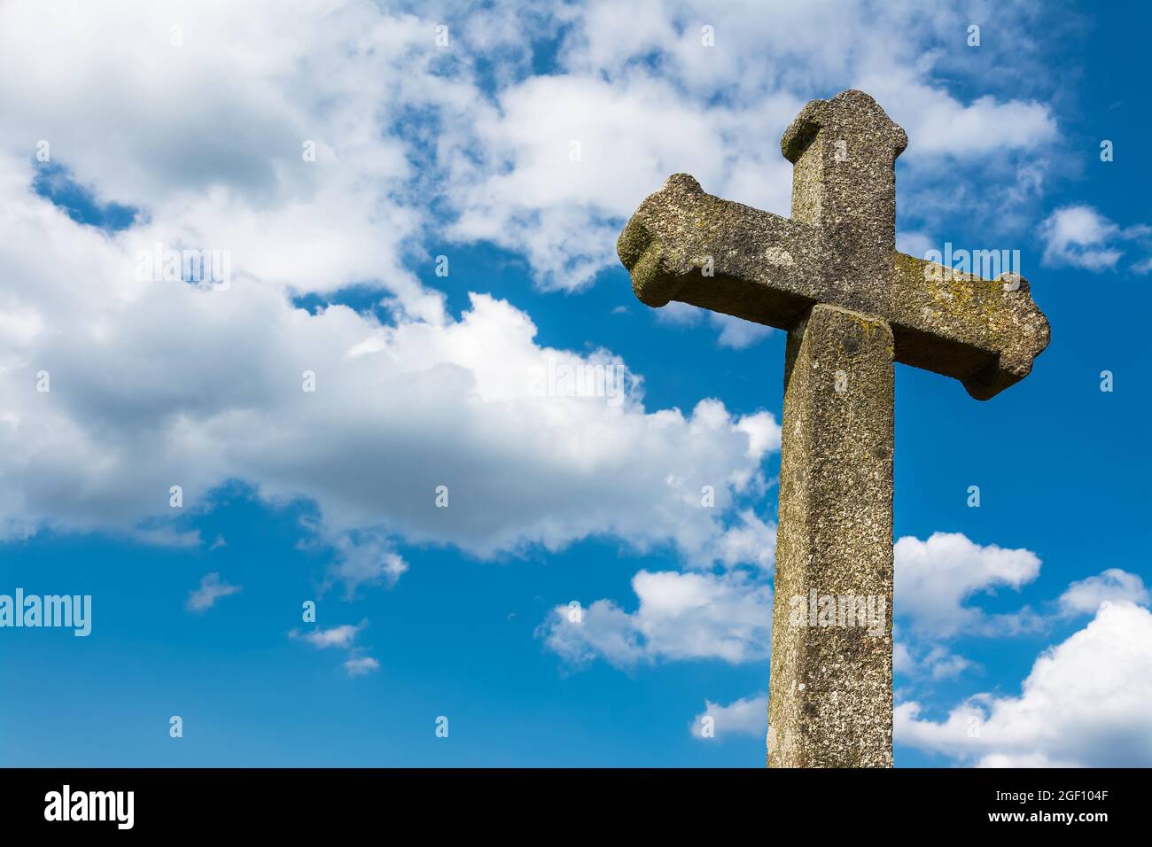 Altes gotisches christliches Steinkreuz auf dramatischem blauem Himmel Hintergrund. Weiße Wolken. Detail des sonnenbeschienenen antiken Kruzifixes. Vintage-Denkmal mit Flechten Abdeckung. Stockfoto