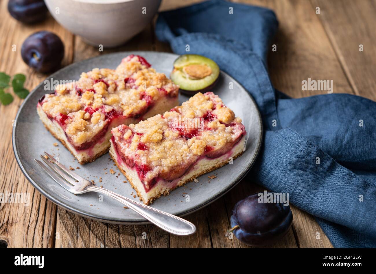 Saftige Pflaumenkuchen-Scheiben mit knuspriger Streusel-Belag auf rustikalem Holzhintergrund Stockfoto