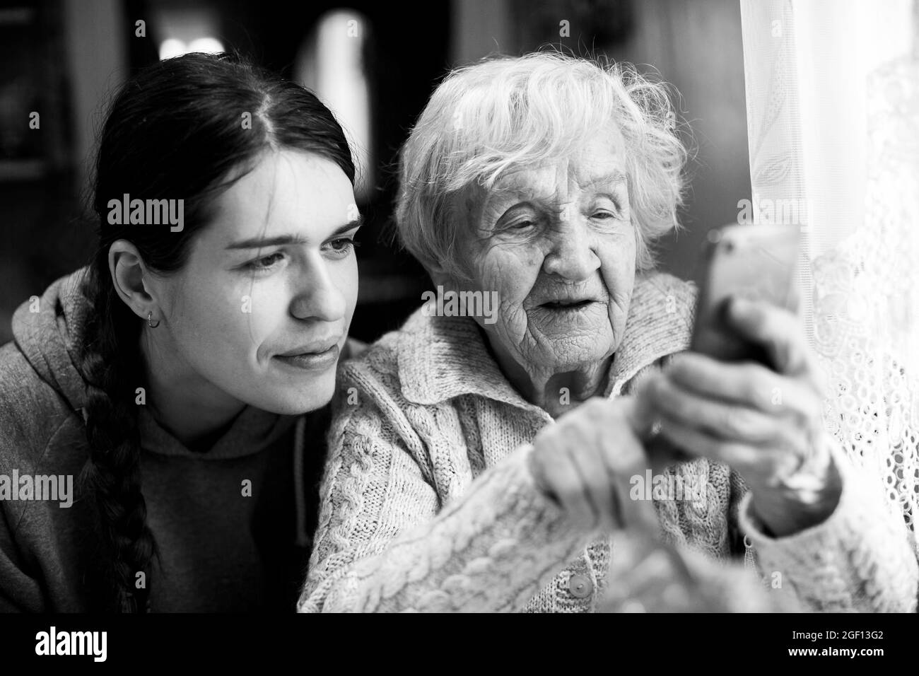 Eine Oma alte Frau schaut mit seiner erwachsenen Enkelin auf ein Smartphone. Schwarzweiß-Foto. Stockfoto