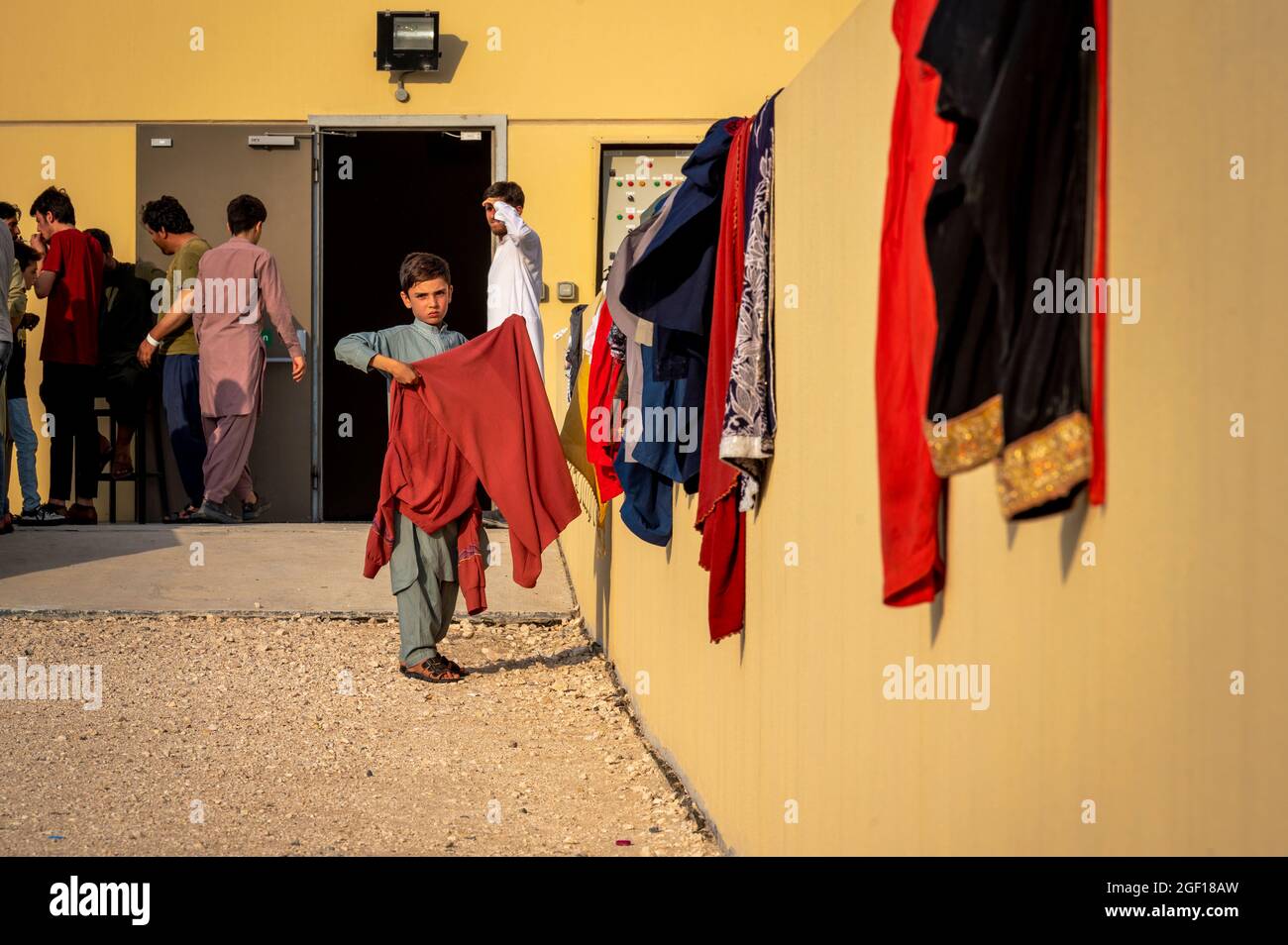 Al Udeied Air Base, Katar. August 2021. Ein afghanischer Junge legt in einer provisorischen Wohnanlage für Flüchtlinge, die am 21. August 2021 auf dem Luftwaffenstützpunkt Al Udied in Katar aus Kabul evakuiert wurden, Wäsche zum Trocknen auf. Quelle: Planetpix/Alamy Live News Stockfoto