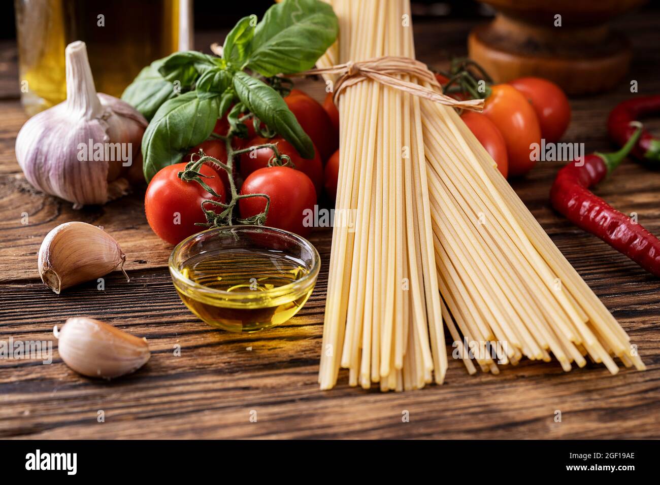 Rohe Pasta Spaghetti mit Tomaten, Knoblauch Olivenöl Basilikum auf alten rustikalen Holzhintergrund Stockfoto