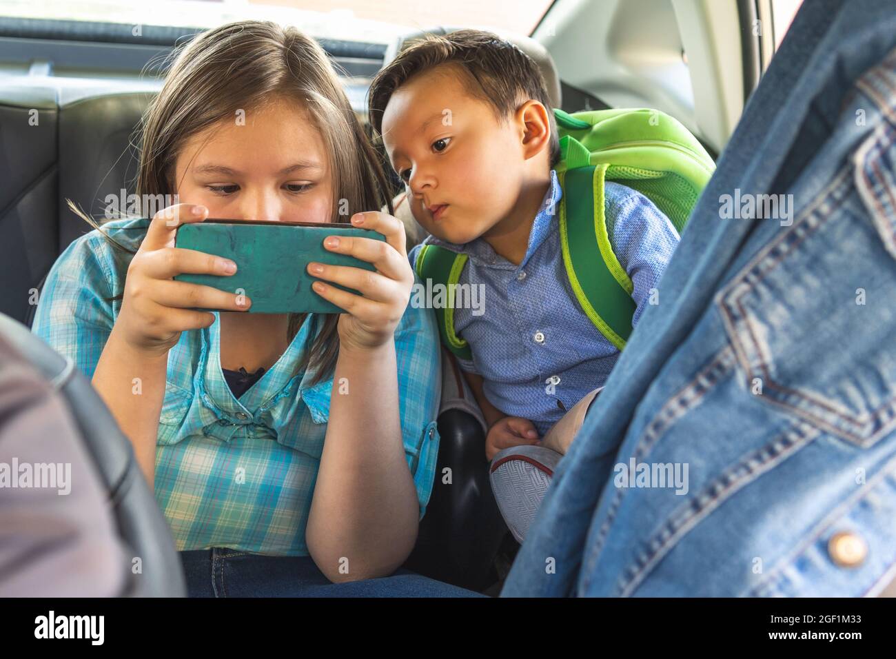 Zwei Kinder schauen auf ein Mobiltelefon auf dem Rücksitz eines Fahrzeugs Stockfoto
