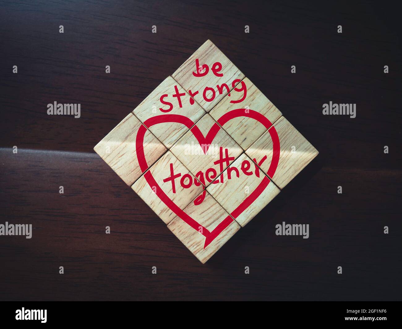 Sei stark und zusammen, Worte und rotes Herz auf hölzernen Würfelblöcken auf dunkelbraunem Holzhintergrund. Stockfoto