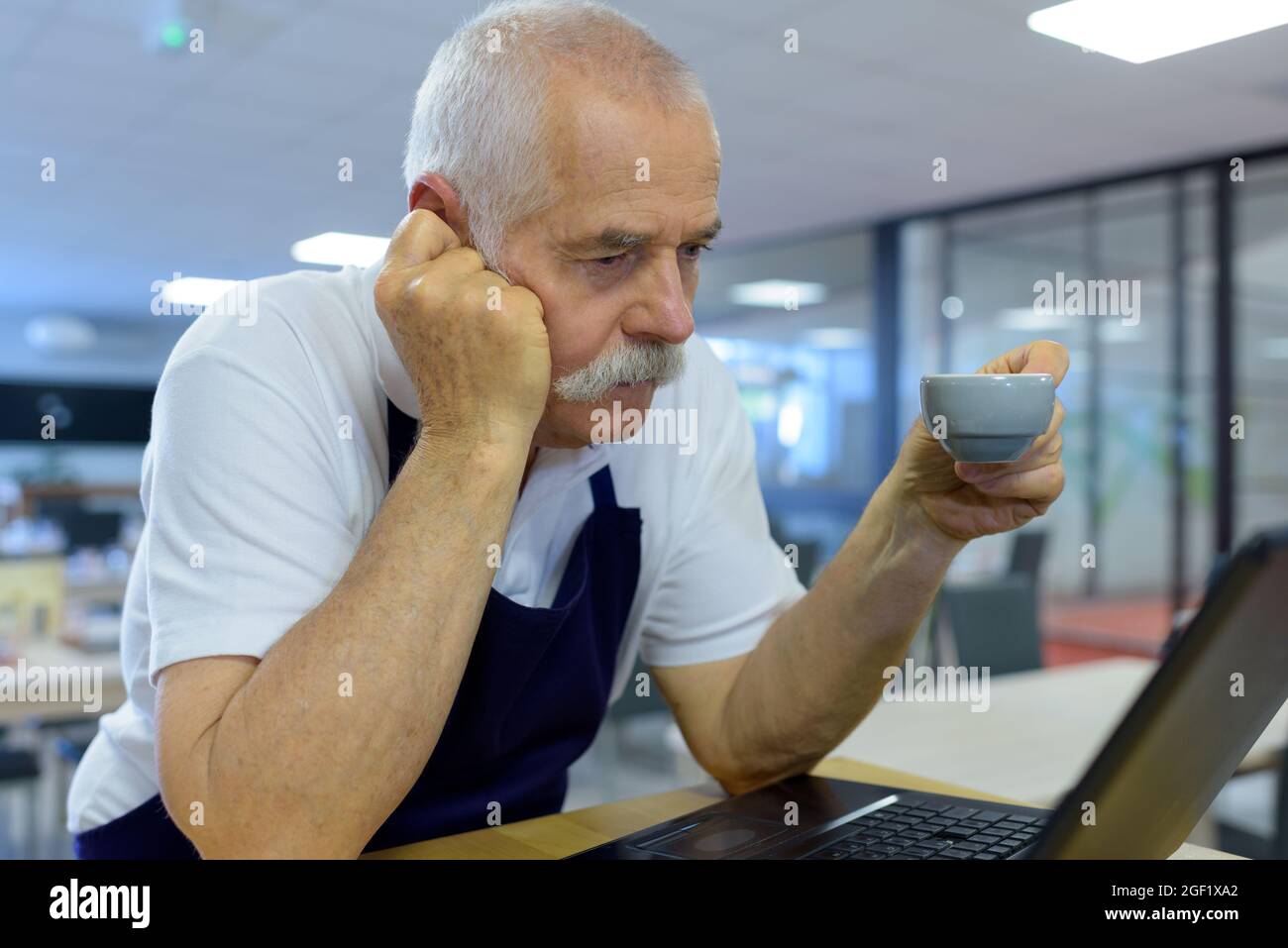 Gelangweilt aussehender, älterer Barista, der von einem Laptop liest Stockfoto