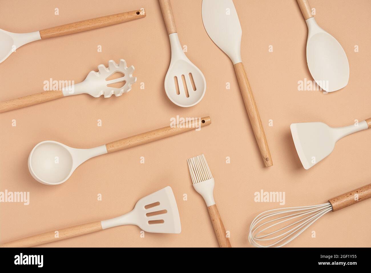 Muster aus Kochgeschirr-Set. Küchengeräte aus Silikon mit Holzgriff auf beigem Hintergrund. Draufsicht Flat Lay. Stockfoto