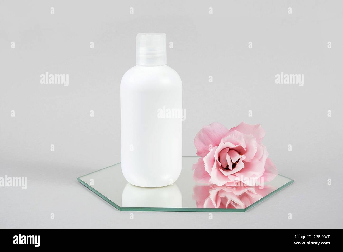 Weiße kosmetische leere Flasche und rosa Blume auf Spiegel, grauer Hintergrund. Natural Organic Spa Kosmetik Schönheitskonzept Mockup, Vorderansicht. Stockfoto