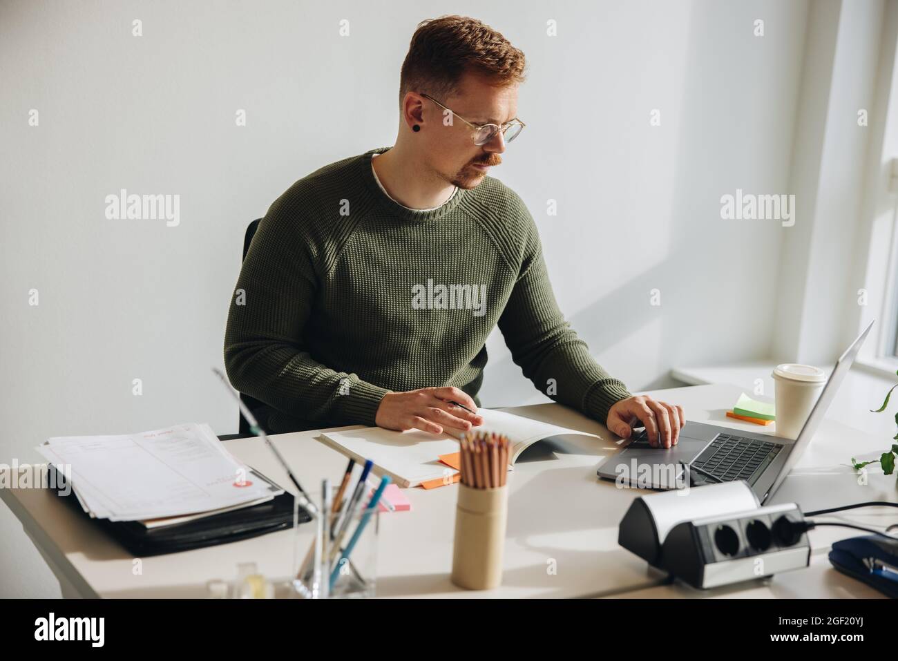 Mann, der an seinem Schreibtisch sitzt, beschäftigt mit der Arbeit am Laptop. Männlicher Unternehmer, der allein an einem Projekt arbeitet. Stockfoto