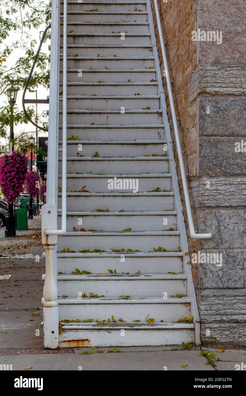 Alte, verwitterte, weiß gestrichene Holztreppe entlang eines attraktiven Steingebäudes in einem städtischen Gehsteig mit hellem Schatten Stockfoto