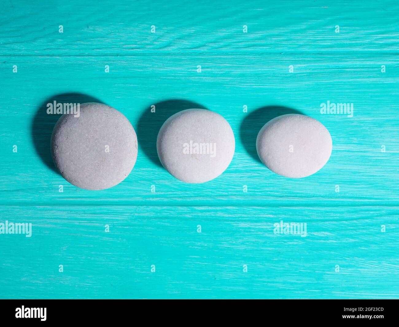 Drei weiße Zen-Steine in einer Reihe in einer Linie auf blauem Hintergrund. Stockfoto