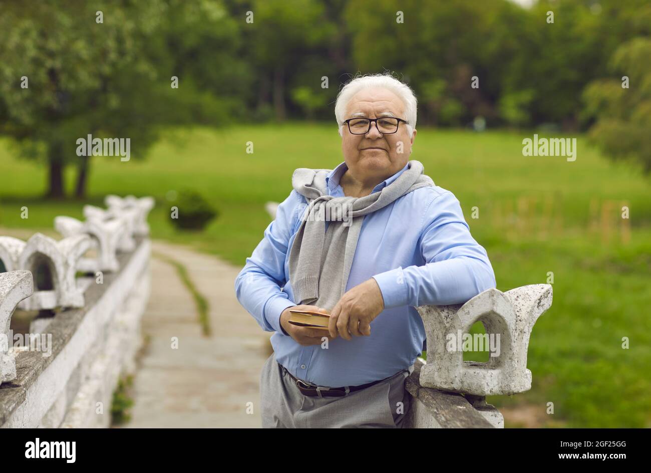 Ein älterer Mann steht mit einem Buch in den Händen im Park. Stockfoto