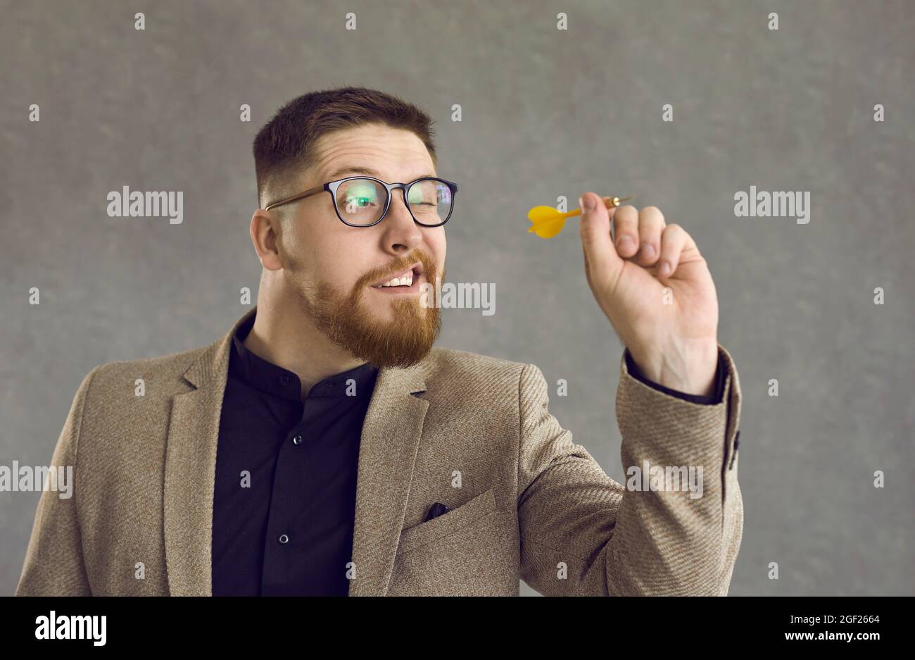 Studio-Porträt eines intelligenten, selbstbewussten jungen Geschäftsmannes, der einen Pfeil auf ein Ziel wirft Stockfoto