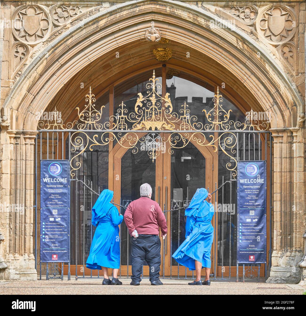 Ein englischer Priester und zwei afrikanische Nonnen am Eingang der christlichen mittelalterlichen Kirche St. Peter in Peterborough, England. Stockfoto