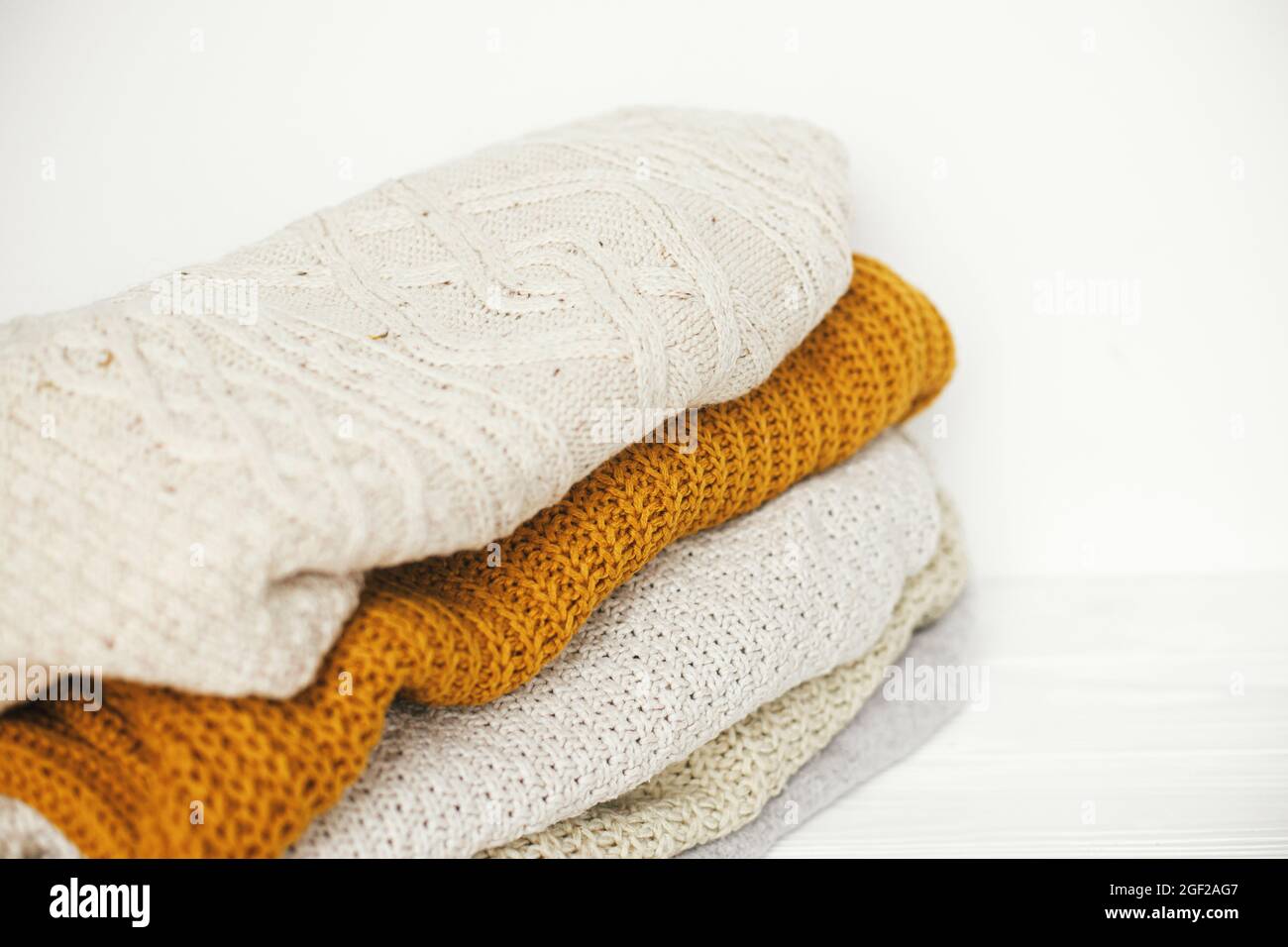 Kuschelige Strickpullover. Ein Haufen weißer, gelber und beigefarbener Pullover aus nächster Nähe im weißen skandinavischen Raum. Hallo Herbst. Stilvolle Garderobe für kalte Meere Stockfoto