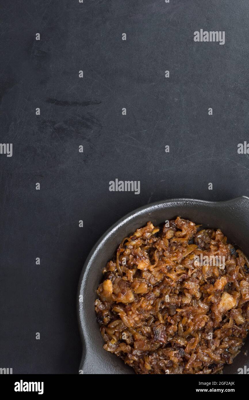 Draufsicht auf karamellisierte Zwiebel auf schwarzem Teller auf schwarzem Hintergrund Stockfoto