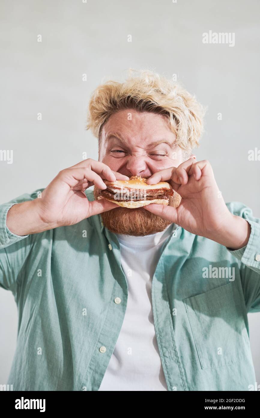 Nahaufnahme von übergewichtigen Mann beißen Burger mit Vergnügen und essen es zum Mittagessen Stockfoto