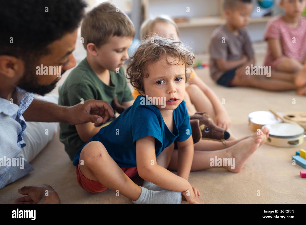 Ein Lehrer, der im Klassenzimmer mit einem kleinen unglücklichen Jungen spricht und ihn tröstet. Stockfoto