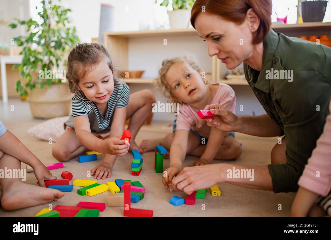 Gruppe von kleinen Kindergarten-Kindern mit Lehrer auf dem Boden drinnen im Klassenzimmer, spielen, Stockfoto