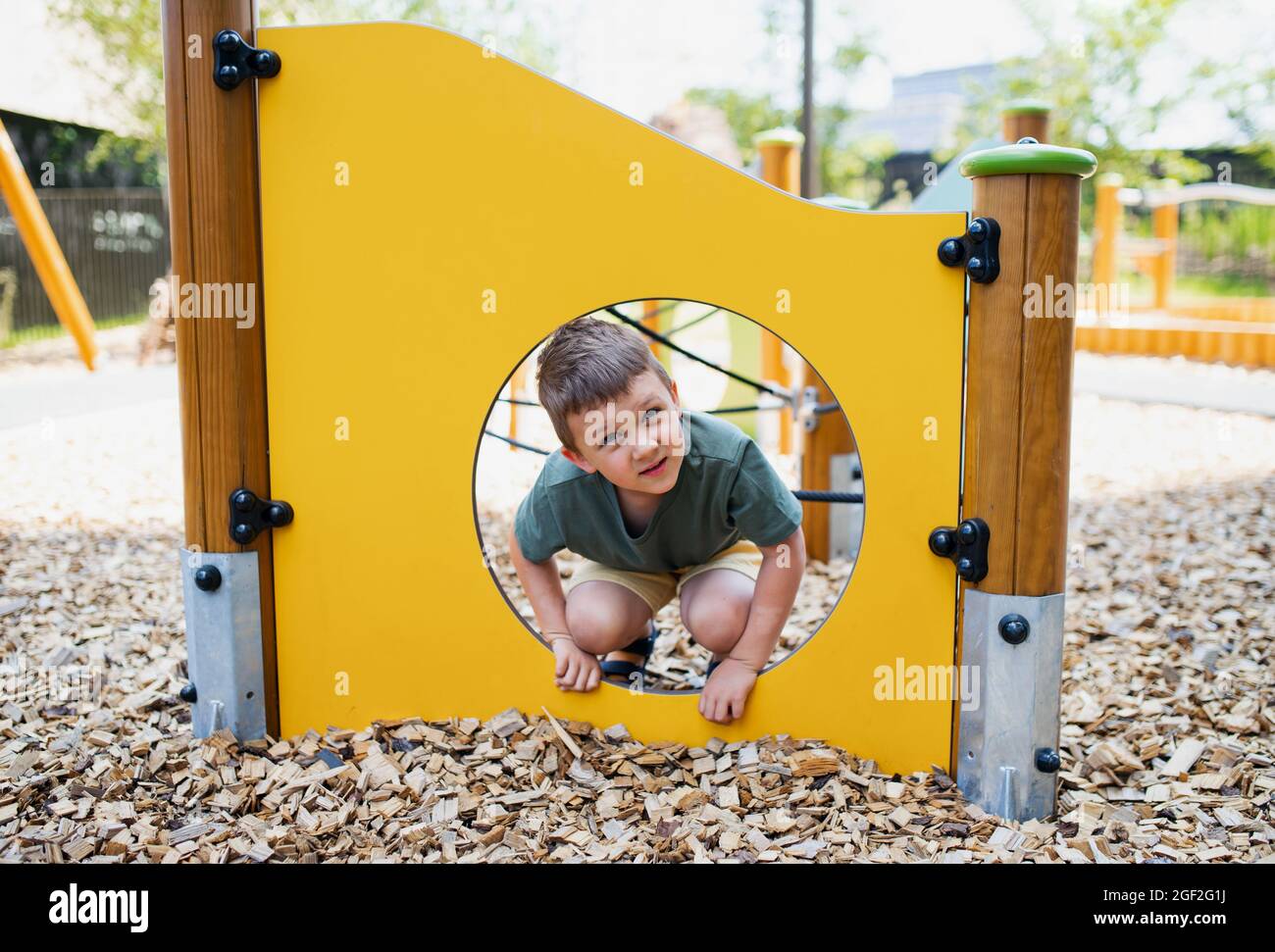 Kleiner Kindergartenjunge, der draußen auf dem Spielplatz spielt und die Kamera anschaut. Stockfoto