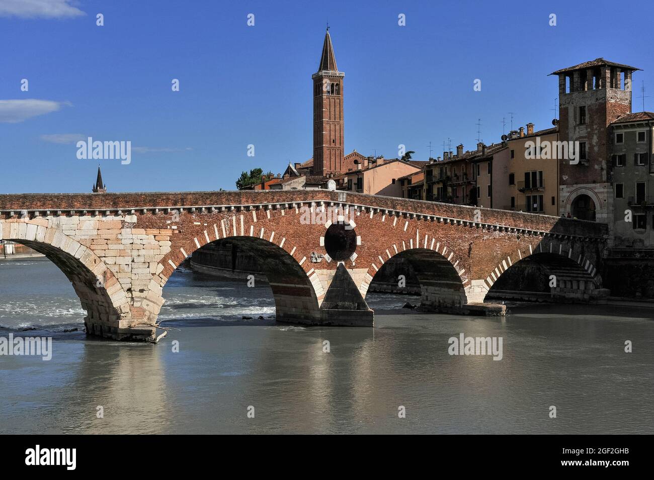 Der Backsteinturm der Kirche Santa Anastasia aus den 1400er Jahren erhebt sich über ein wichtiges römisches Denkmal in Verona, Veneto, Italien: Die Eselbrücke Ponte della Pietra, die die alpine Etsch überspannt. Der ursprüngliche Pons Marmoreus trug die befahrene Via Postumia, die Verona mit den Städten im äußersten Westen und Osten Italiens verband, brach aber oft bei Überschwemmungen zusammen und wurde teilweise aus Ziegeln wiederaufgebaut. Rückläufige deutsche Truppen sprengten 1945 vier der fünf Bögen in die Luft. Die heutige Brücke, die in den 1950er Jahren umgebaut wurde, hat zwei östliche Römerbögen, zwei venezianische Bögen aus dem 16. Jahrhundert und einen westlichen Bogen, der 1298 umgebaut wurde. Stockfoto