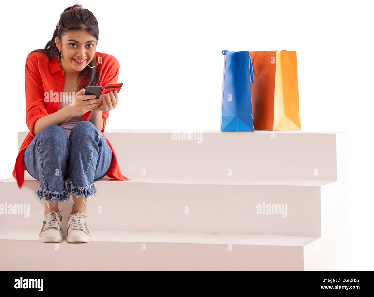 Eine junge Frau, die online mit Kreditkarte und Handy mit Einkaufstaschen zurückgehalten bezahlen. Stockfoto