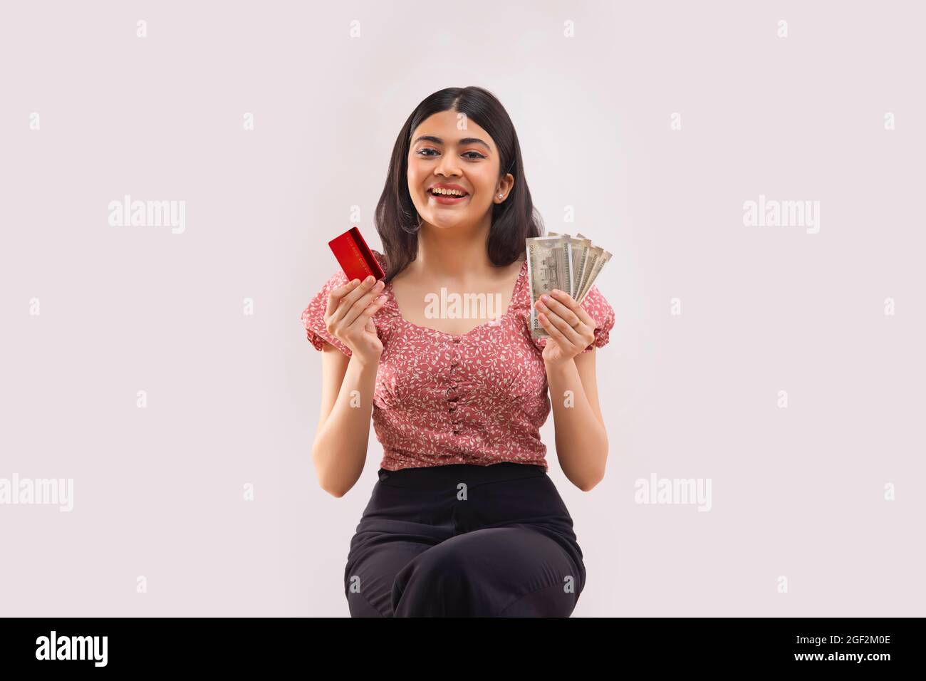 Porträt einer jungen Frau, die in jeder Hand mit Kreditkarte und Bargeld sitzt. Stockfoto