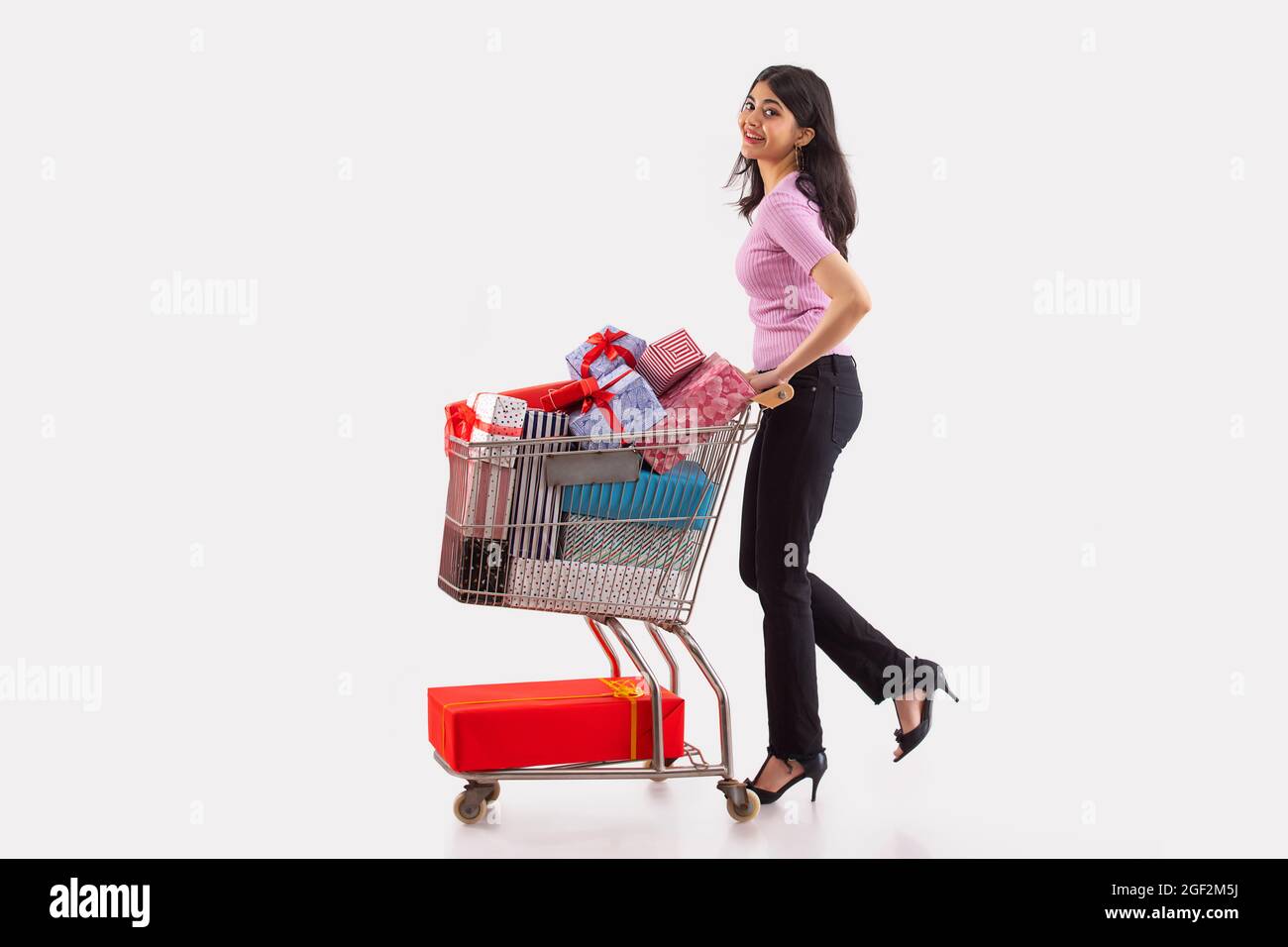 Porträt einer jungen Frau, die einen Wagen voller Geschenkschachteln bewegt. Stockfoto